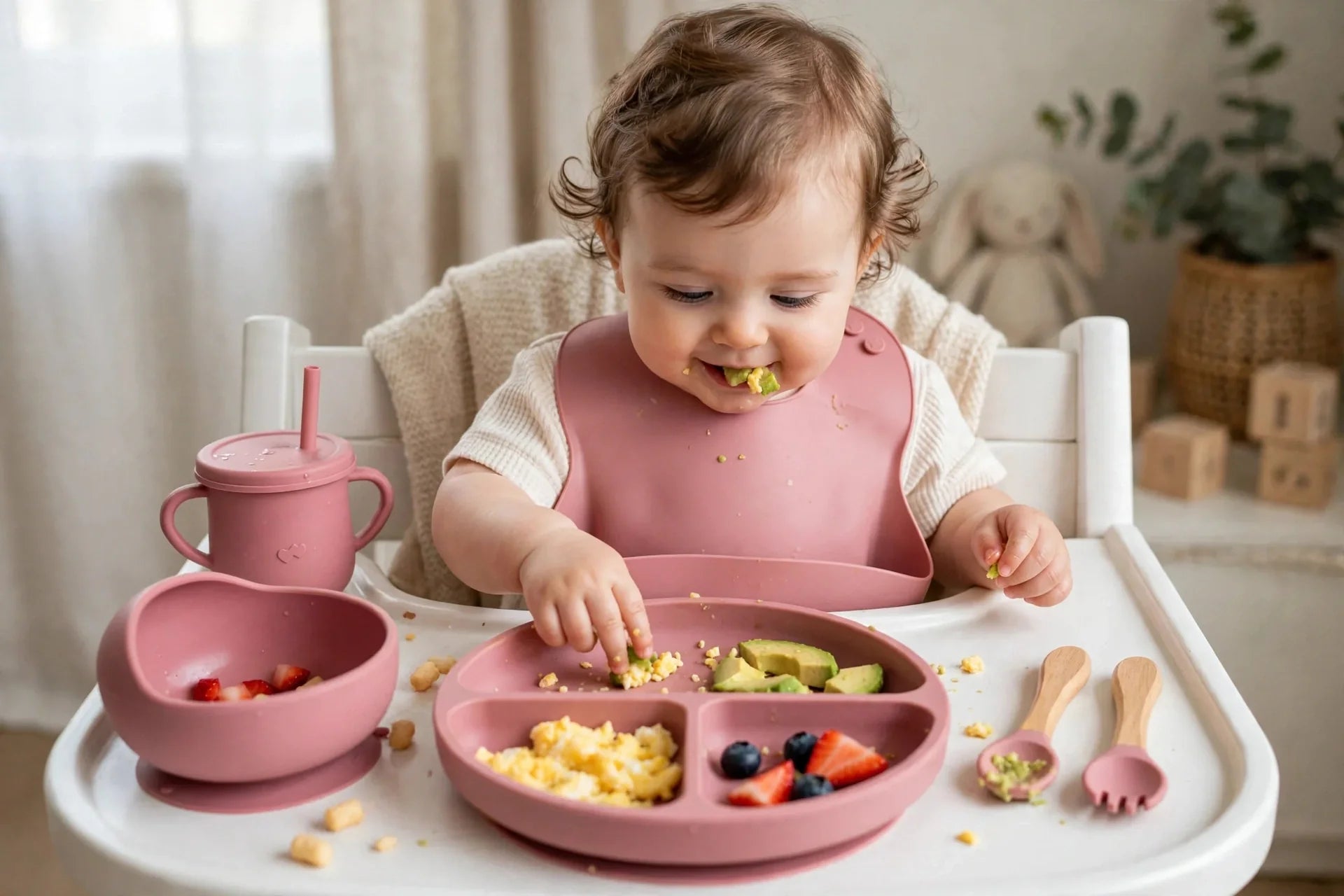 Pink silicone baby feeding set on high chair tray with bib, plate, cup and utensils